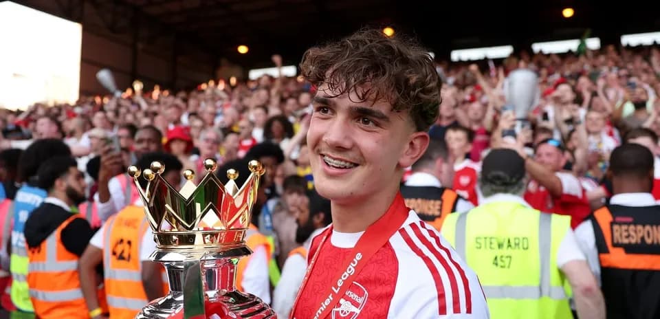 Player holding Premier League trophy with celebrating crowd