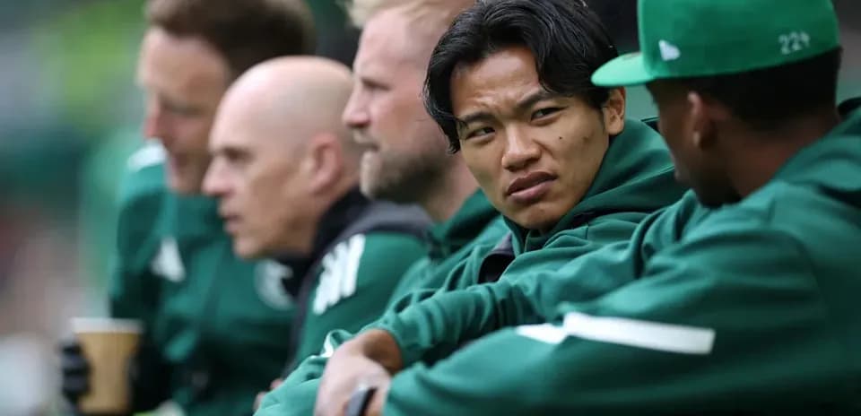 Players sitting on bench during match, wearing team jackets