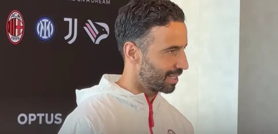 Man speaking during press conference with team logos
