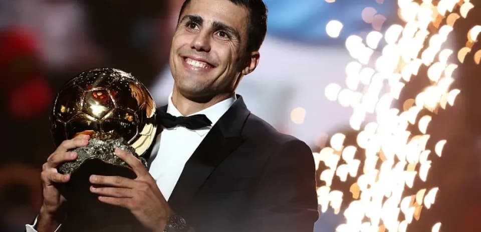 Player celebrating with Ballon d'Or trophy on stage