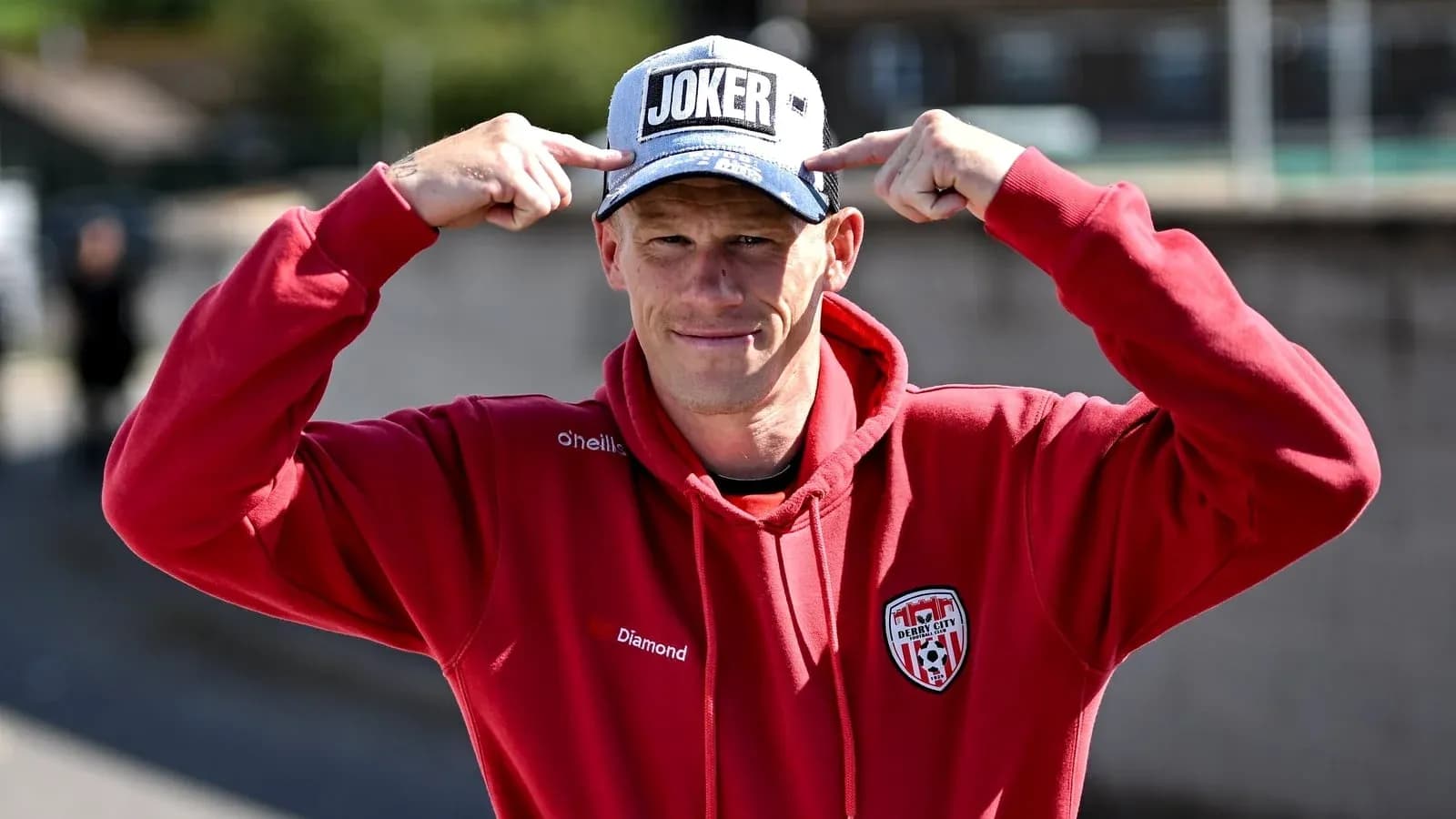 Person wearing a 'JOKER' cap and red hoodie