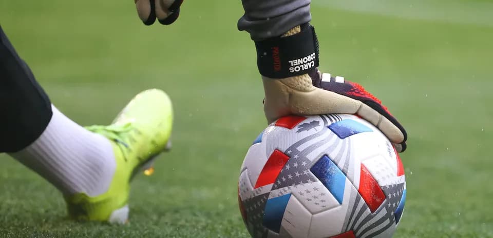 Goalkeeper placing hand on soccer ball on field