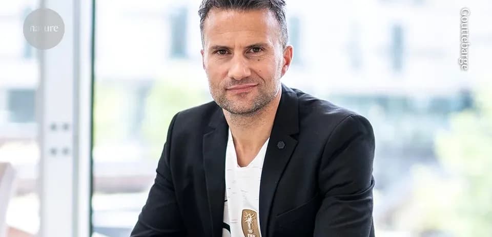 Man in black blazer seated indoors, smiling