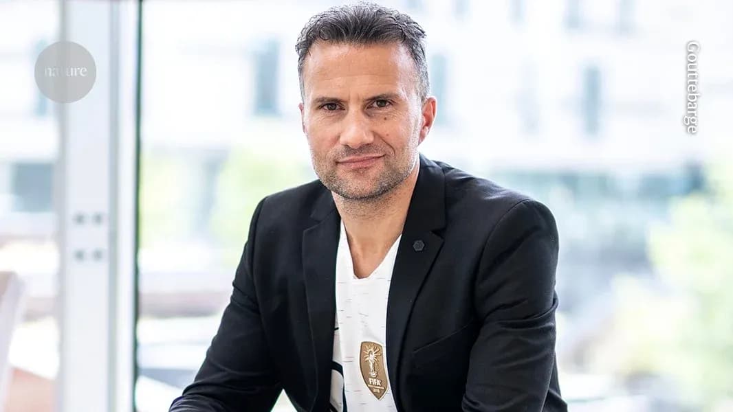 Man in black blazer seated indoors, smiling