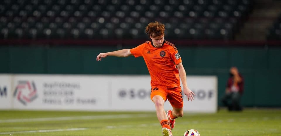 Player in orange kit kicking soccer ball