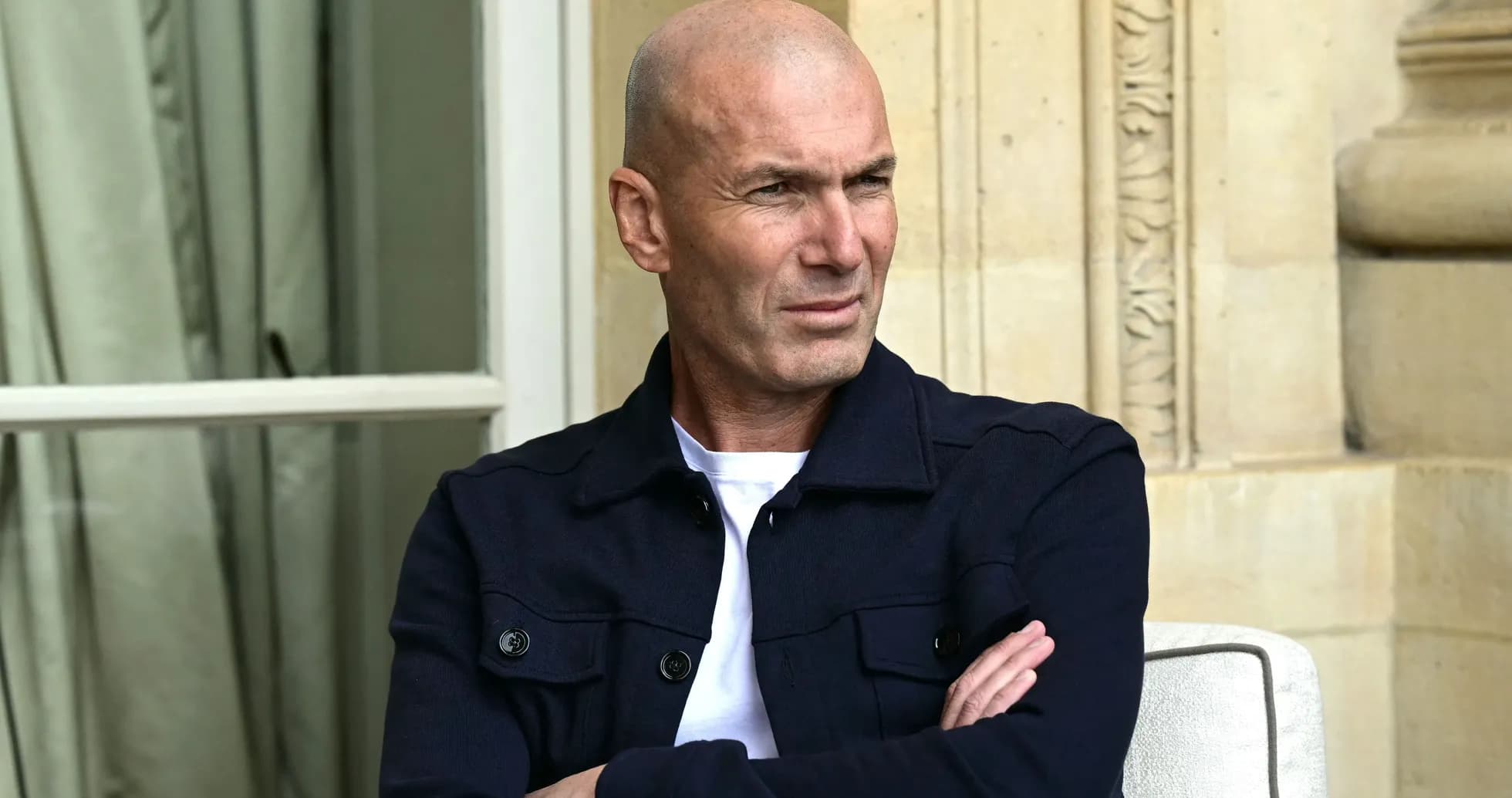 Man sitting with arms crossed, wearing dark jacket