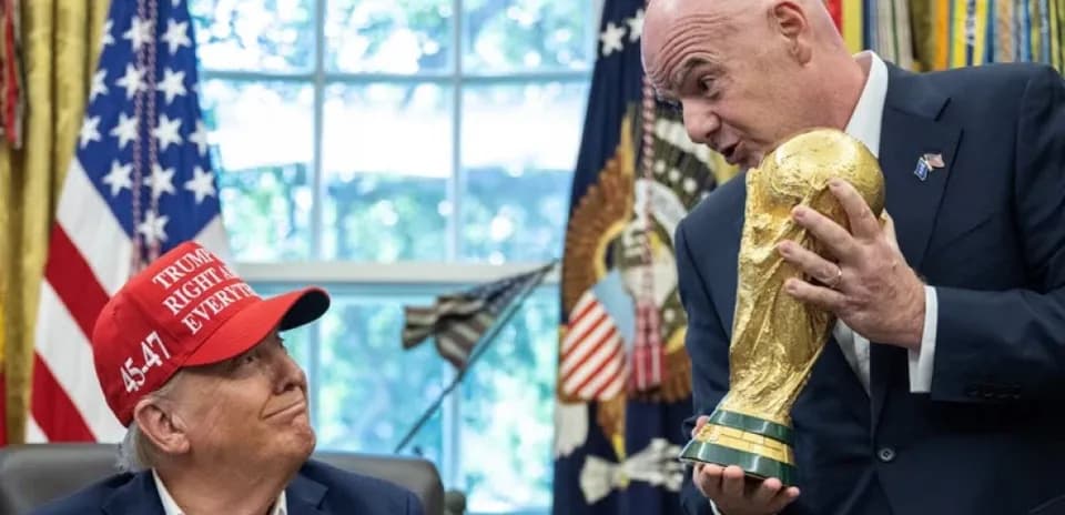 Person holding FIFA World Cup trophy with another seated