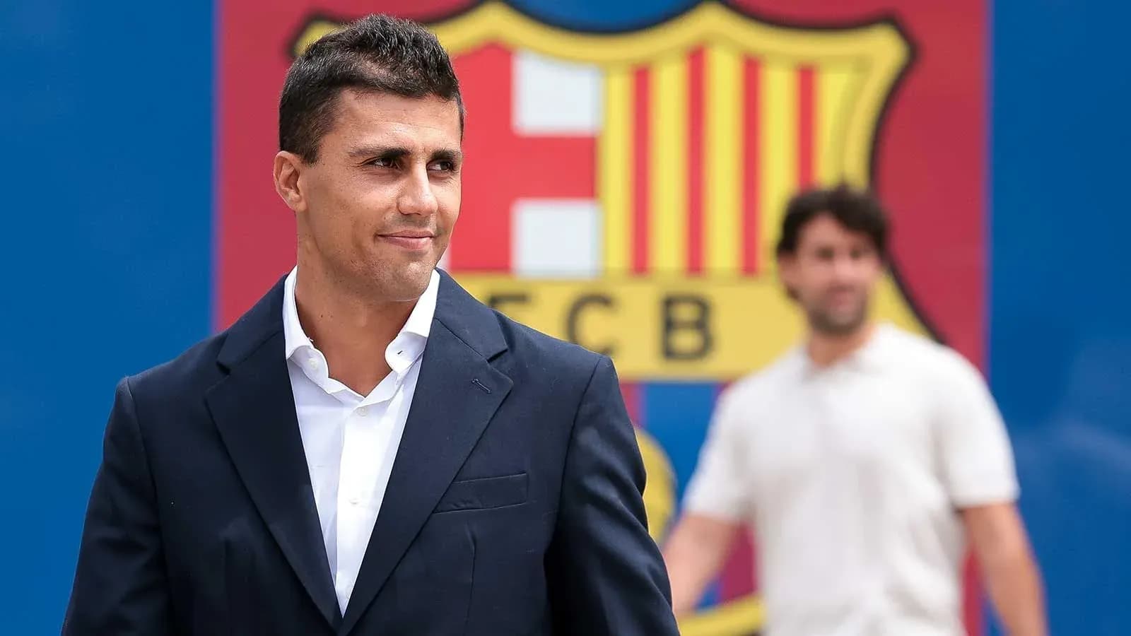 Man in suit standing in front of FC Barcelona logo