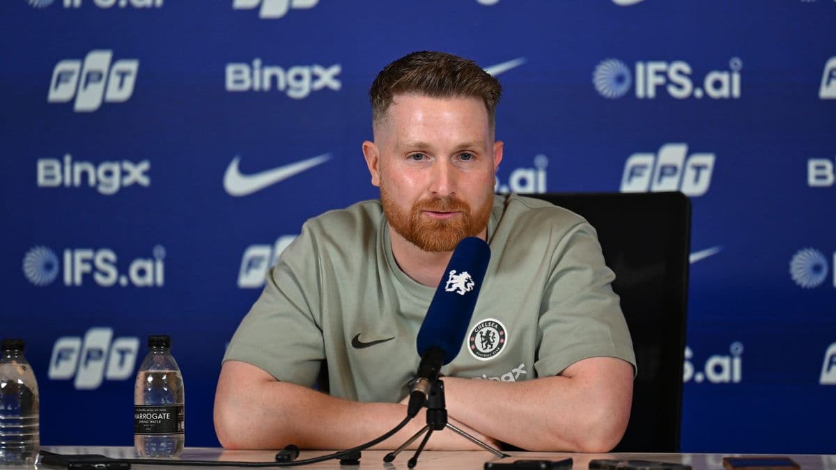 Man speaking at press conference with Chelsea branding