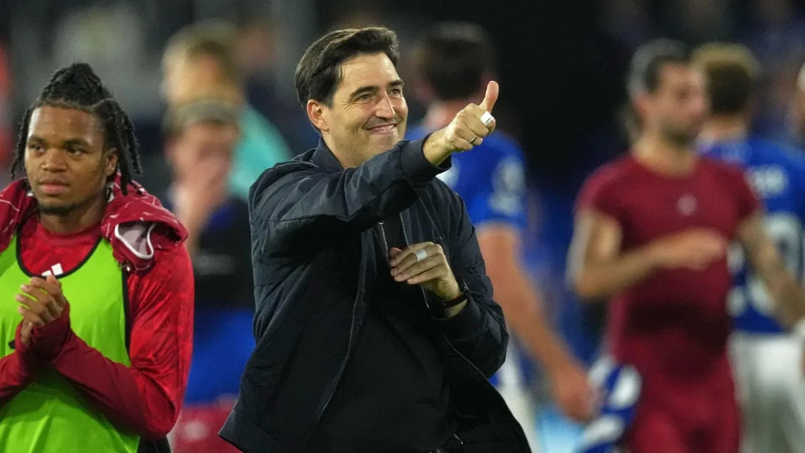 Coach giving thumbs up with players in background