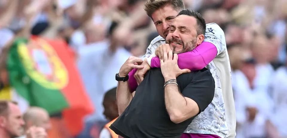 Two coaches celebrating with a hug on the field