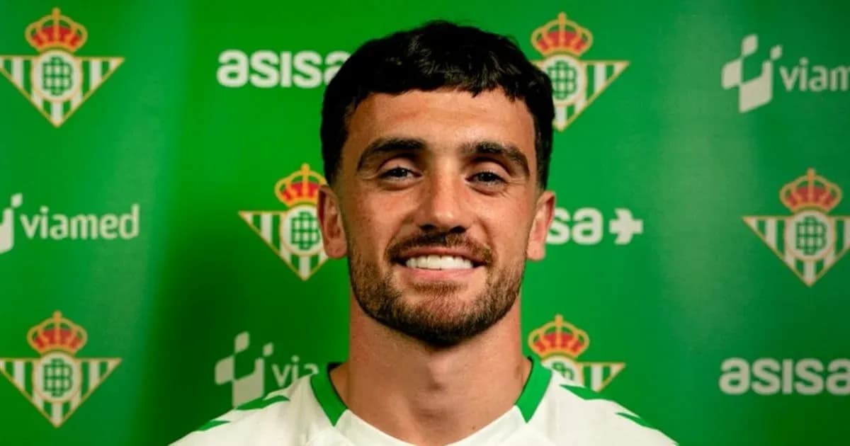 Football player posing in club kit with logo backdrop