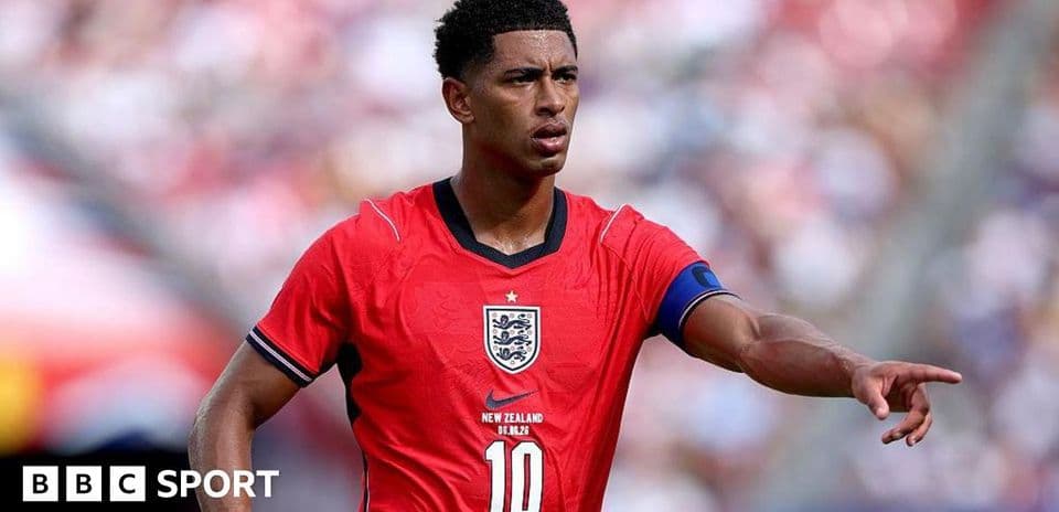 Player in red England kit directing teammates on field