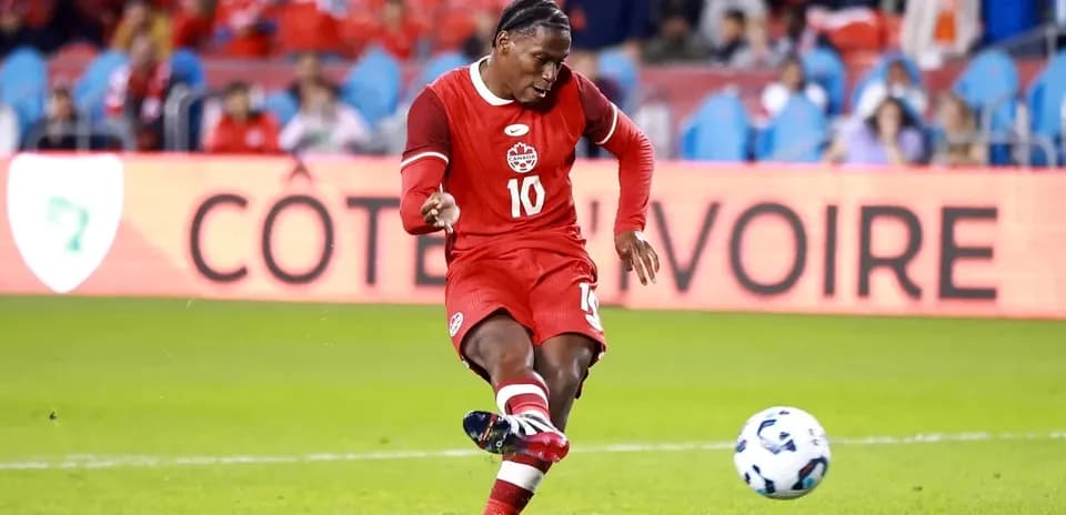 Player in red kit kicking soccer ball on field
