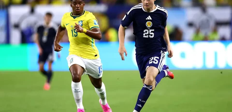 Player from Scotland dribbling ball, Brazilian defender chasing