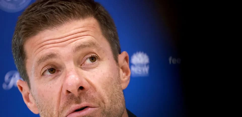 Coach speaking at press conference with blue backdrop