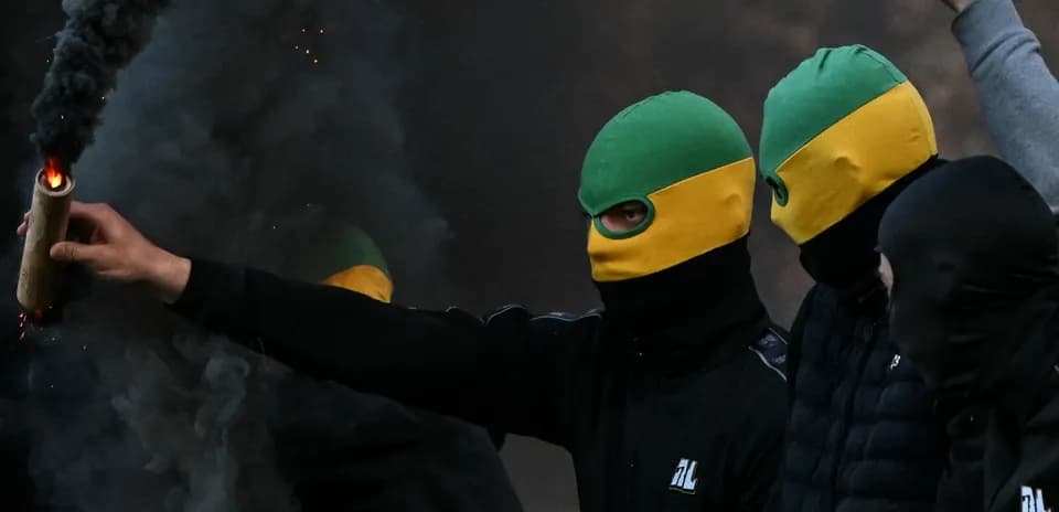 Masked individuals holding flares in smoke-filled area