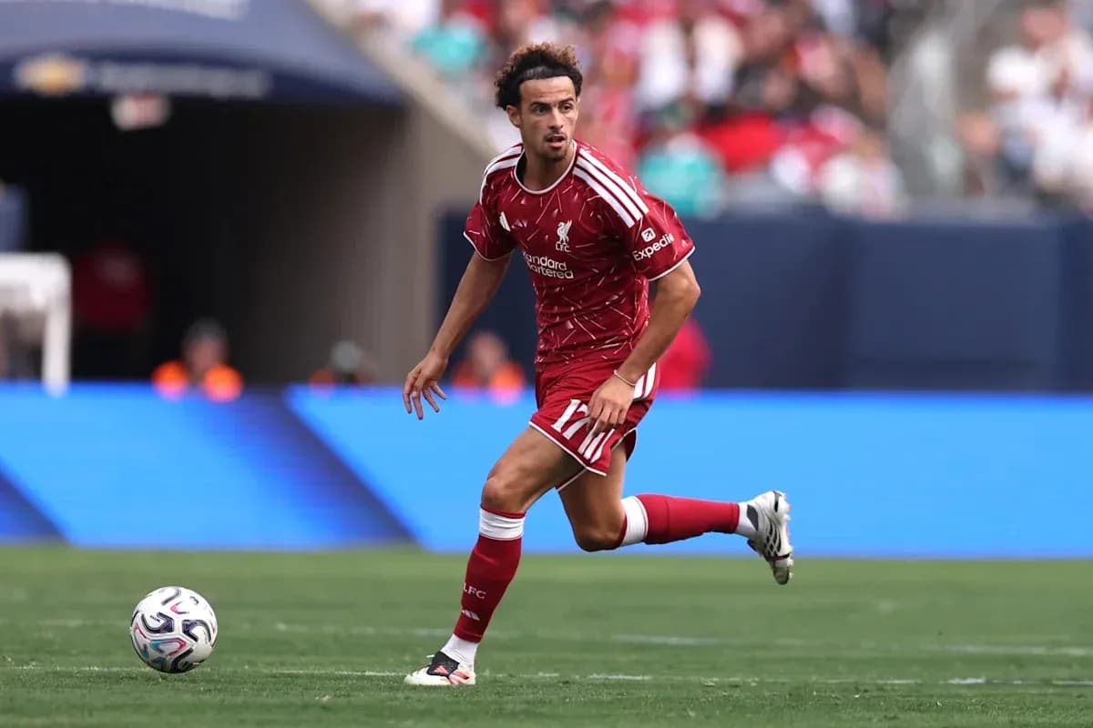 Player in red kit dribbling ball on field Player in red kit dribbling ball on field