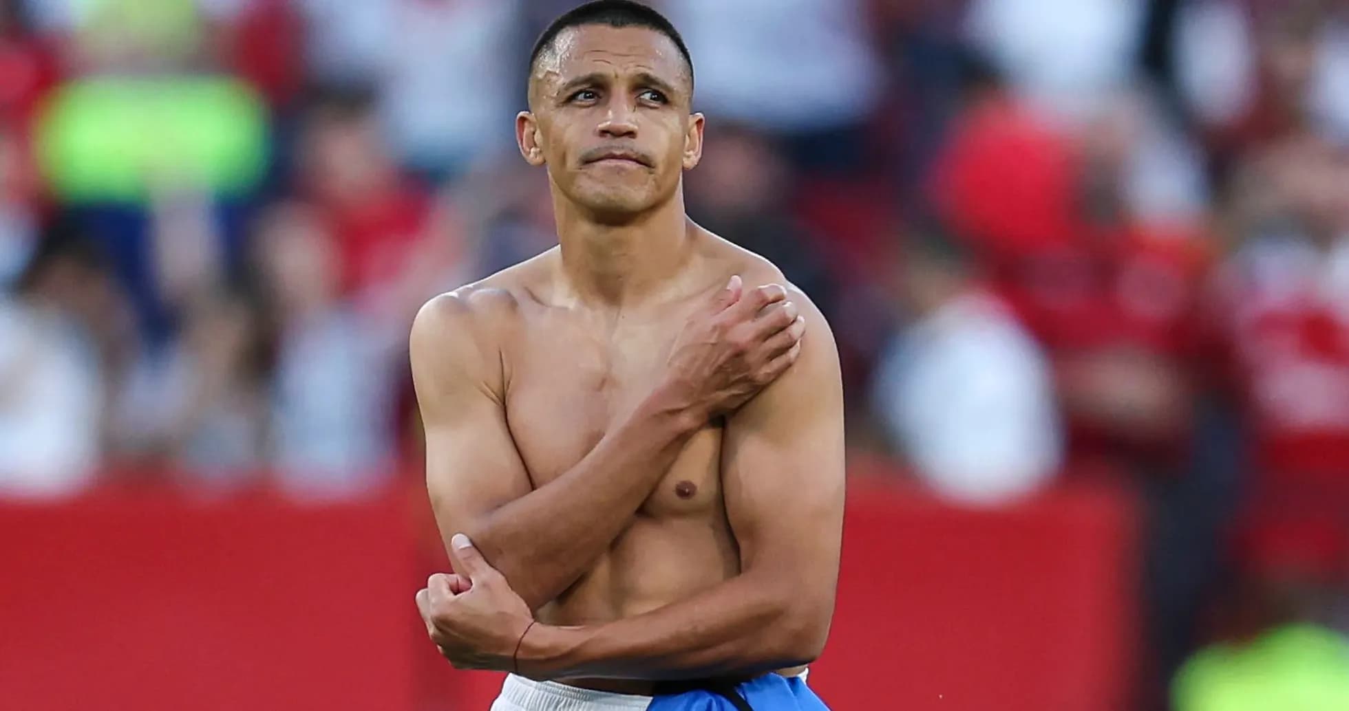 Player standing shirtless with blue shorts on field Player standing shirtless with blue shorts on field