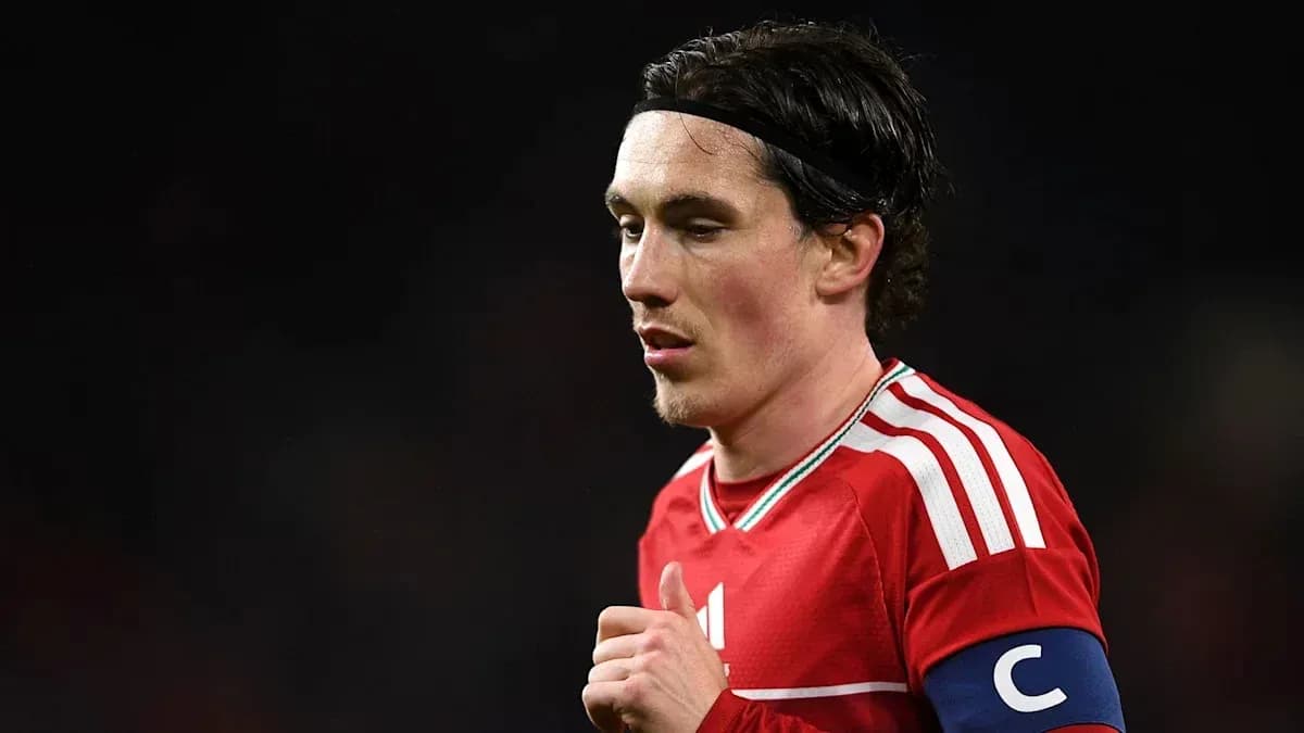 Player in red jersey with captain's armband on field Player in red jersey with captain's armband on field