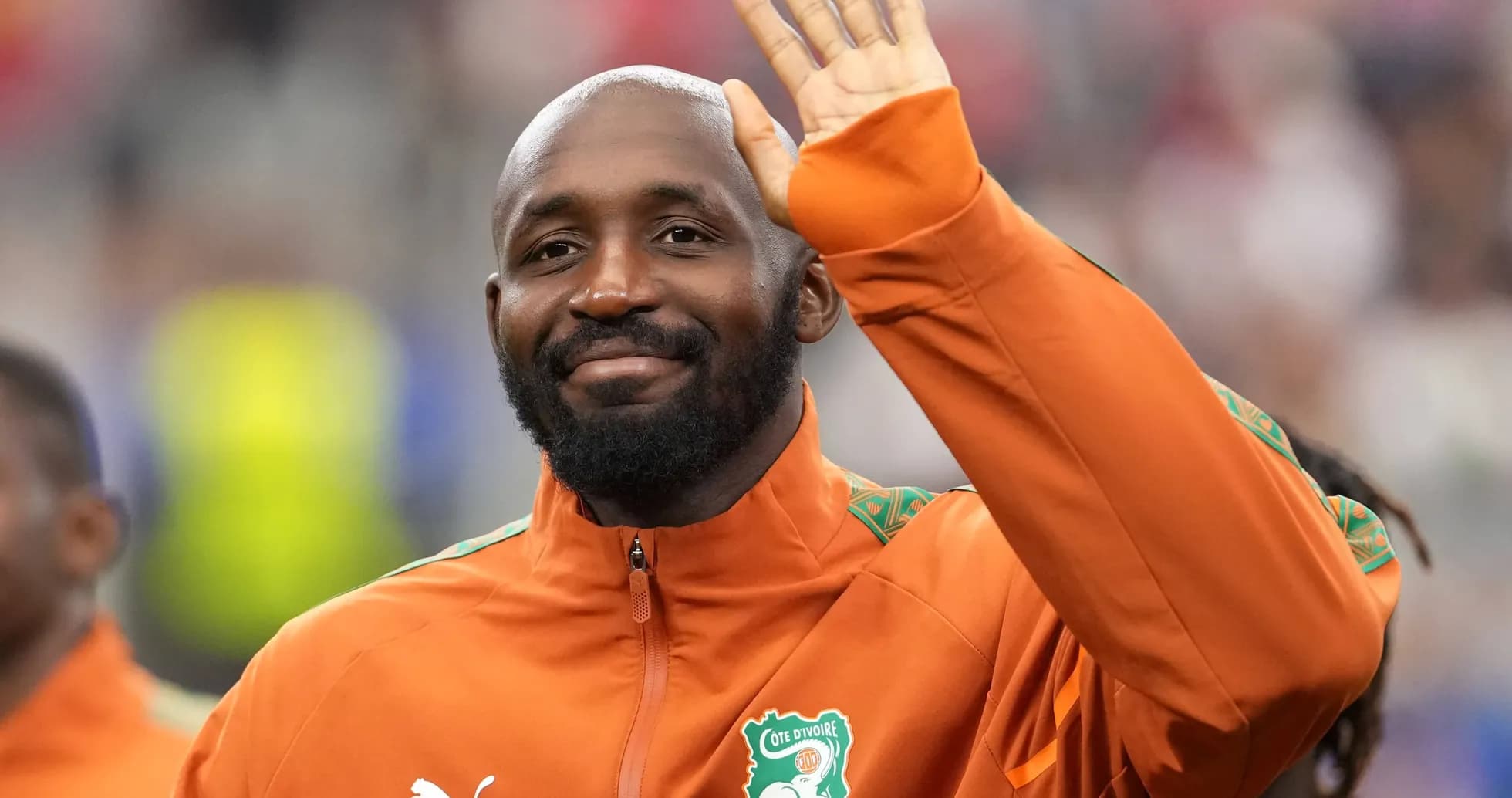 Player waving during pre-match warm-up in orange jacket Player waving during pre-match warm-up in orange jacket