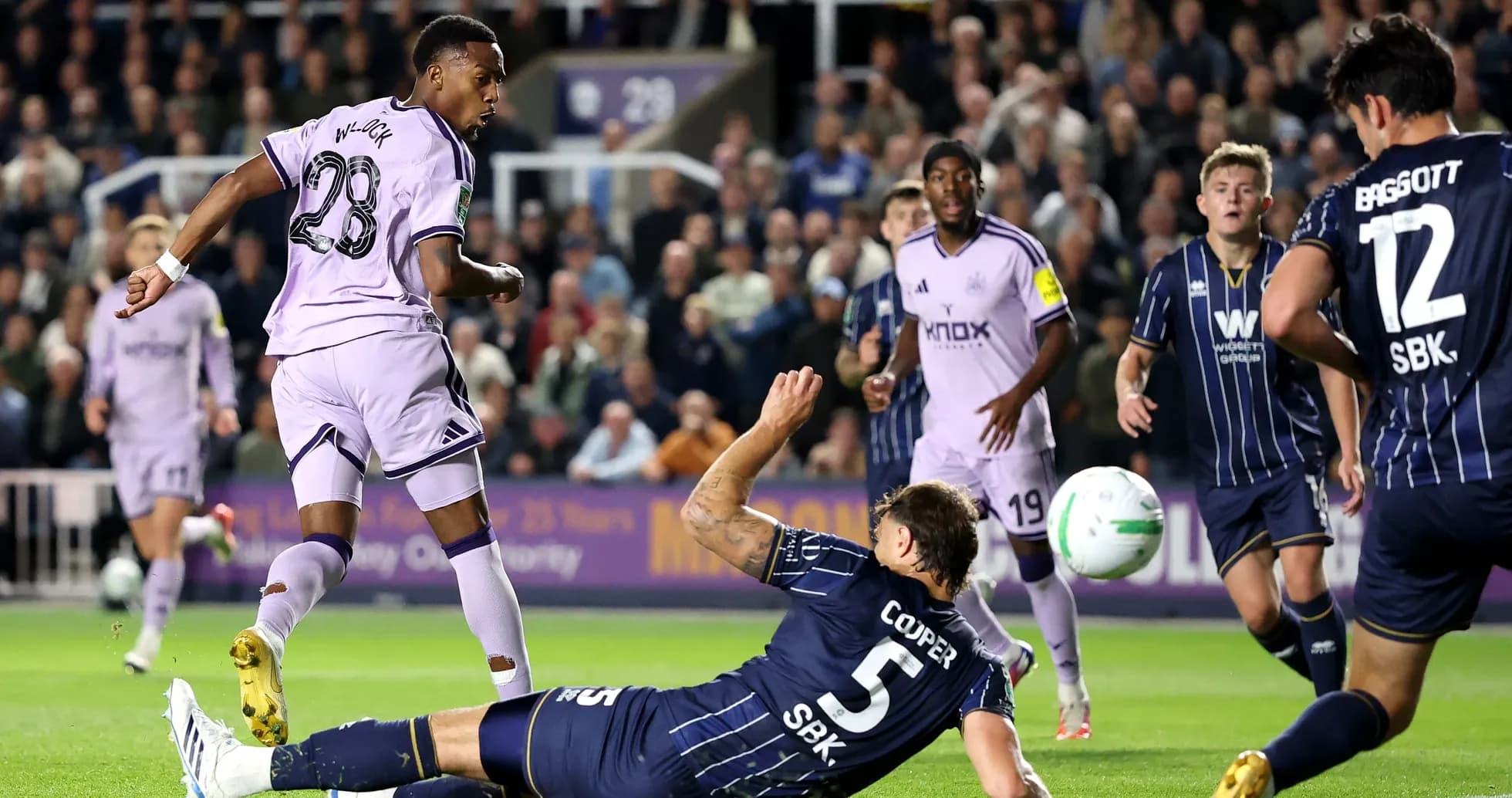 Player in purple kit shooting while defender falls Player in purple kit shooting while defender falls