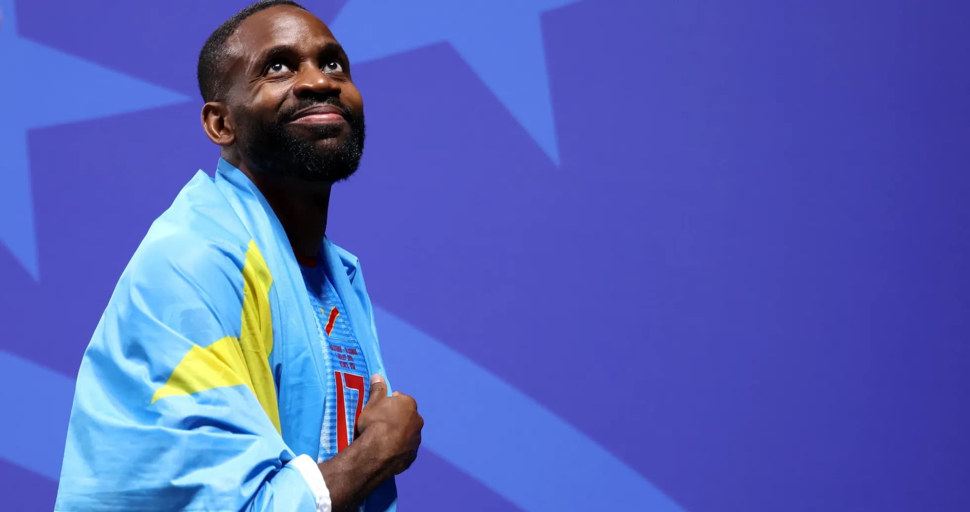 Athlete wearing flag, looking up at event backdrop Athlete wearing flag, looking up at event backdrop
